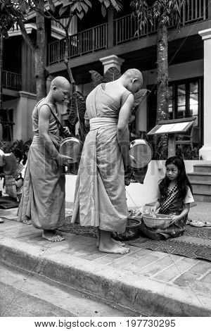 LUANG PRABANG LAOS - MARCH 12 2017: Black and white and vertical picture of Buddhist Alms Giving Ceremony where local people offers food and money before the sunrise in Luang Prabang Laos.