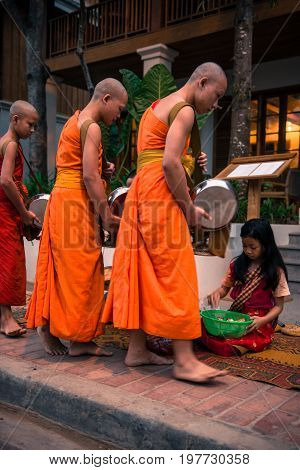 LUANG PRABANG LAOS - MARCH 12 2017: Vertical picture of Buddhist Alms Giving Ceremony where local people offers food and money before the sunrise in Luang Prabang Laos.