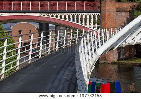 The modern Merchant's Bridge in Castlefield Basin with the historical Victorian Rail Viaduct behind.