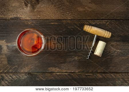 Photo of old-fashioned corkscrew with cork, shot from above on dark wooden background texture with glass of rose wine and place for text. Design template for wine list or tasting invitation