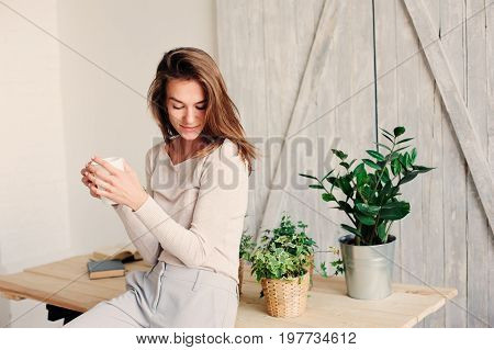 beautiful young feminine woman relaxing at home in lazy weekend morning with cup of coffee wearing casual fashion clothes
