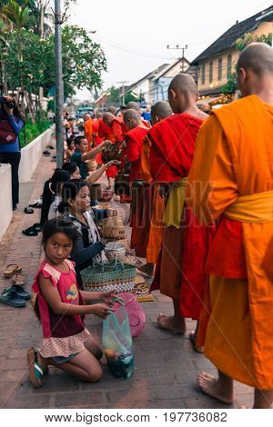 LUANG PRABANG LAOS - MARCH 12 2017: Vertical picture of local people giving food and money to the monks for the Buddhist Alms Giving Ceremony in Luang Prabang Laos.