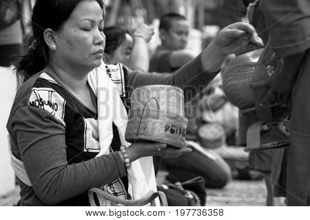 LUANG PRABANG LAOS - MARCH 12 2017: Black and white picture of Lao woman giving food for the Buddhist Alms Giving Ceremony before the sunrise in Luang Prabang Laos.