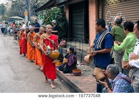 LUANG PRABANG LAOS - MARCH 12 2017: Local people giving food and money to the monks for the Buddhist Alms Giving Ceremony in Luang Prabang Laos. Tourists take photos.