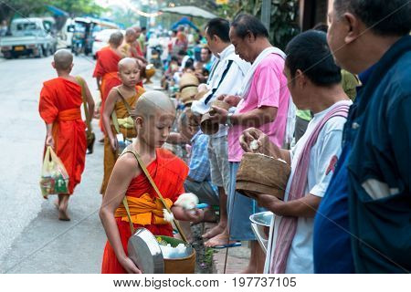 LUANG PRABANG LAOS - MARCH 12 2017: Horizontal picture of local people giving food and money to the monks for the Buddhist Alms Giving Ceremony in Luang Prabang Laos.