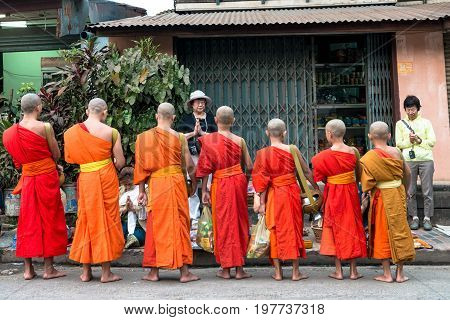 LUANG PRABANG LAOS - MARCH 12 2017: From back Monks in line receiving food for the Buddhist Alms Giving Ceremony in Luang Prabang Laos.