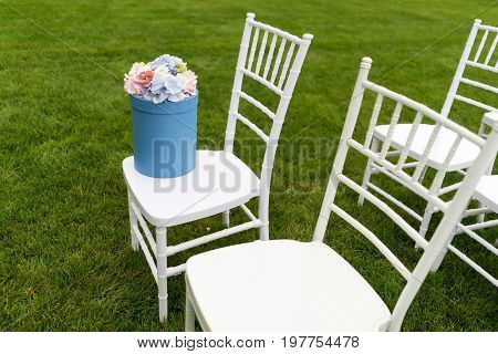 Chiavari chairs on grass. On one of the chairs is a hat box with flowers.