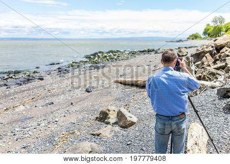 Photographer taking pictures of rocks and Saint Lawrence river in Saint-Irenee Quebec Canada in Charlevoix region with beach