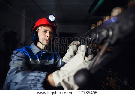 young coal miner is underground in a mine for coal mining in overalls against the backdrop of mining equipment. concept of repair of industrial equipment.