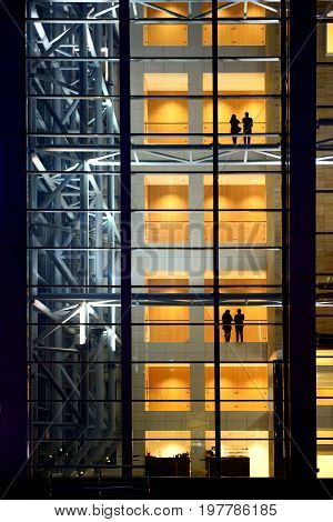 People silhouettes in modern construction glass and steel building in night