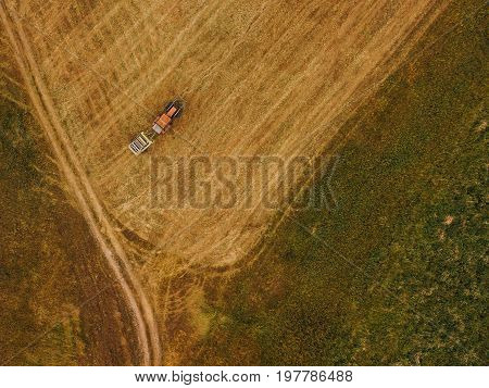 Aerial view of tractor making hay bale rolls in field after wheat harvest drone pov