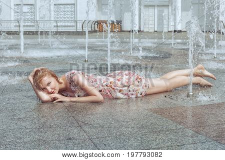 Woman lies in a city fountain and flirts she is all wet and happy.
