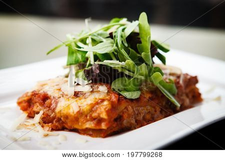 Lasagna served on a white plate with salad