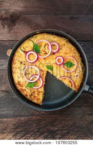 An overhead photo of a Spanish tortilla with potatoes and zucchinis in a tortillera, with a missing slice, and a place for text