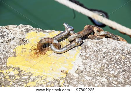 Rusty metal shackle on a metal bar laying on weathered wood outdoors