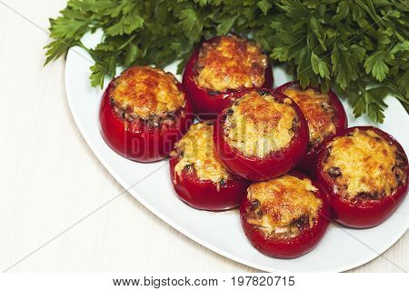 Stuffed mushrooms tomatoes with cheese baked in the oven on a background of green parsley. Healthy diet. A delicious vegetarian dish.