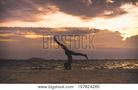 Young woman yoga exersice posting silhouette on the beach in summer