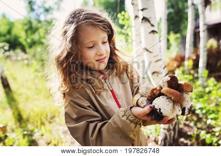 happy child girl picking wild mushrooms on the walk in summer or autumn forest