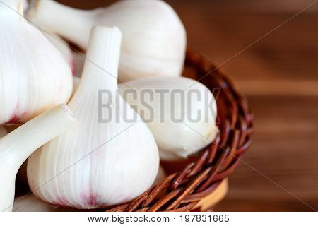 Raw garlic in a basket on a brown wooden background. Harvesting garlic bulbs concept. Fresh garlic background. Closeup