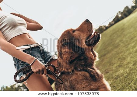 Relaxing in park. Close-up of young woman standing with her dog while spending time outdoors