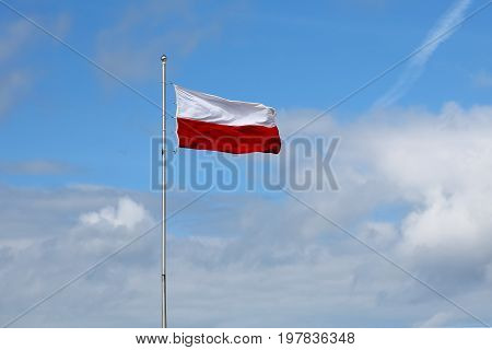 The Polish flag mounted on a high mast is seen on a windy day against the blue sky