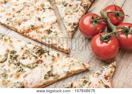 Pieces of pizza and cherry tomatoes on a branch on a light wooden background