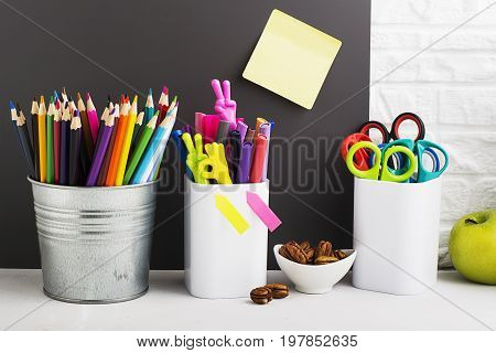 School background: a white brick wall with accessories, pencils, tetrads, scissors, an apple, pecans, a board for a substitute placed in front of her on the table. Selective focus