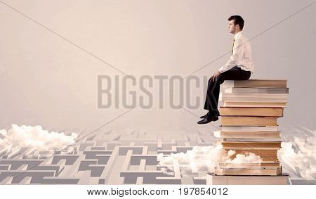 A serious businessman in suit sitting on a pile of giant books in front of a grey wall with clouds, labirynth