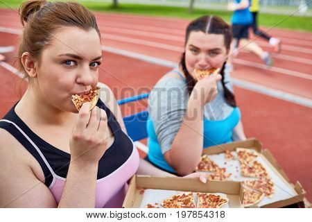 Hungry obese women eating delicious takeout pizza after physical training