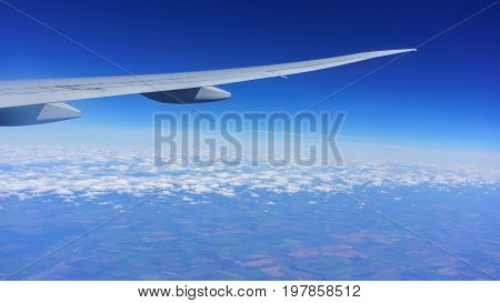 Looking thru airplane 's window seeing wing of airplane white clouds blue sky and land of Moscow Russia