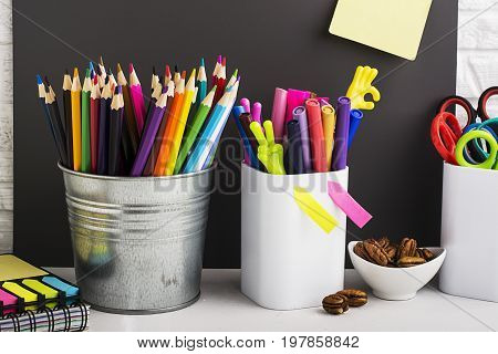 School background: a white brick wall with accessories, pencils, tetrads, scissors, an apple, pecans, a board for a substitute placed in front of her on the table. Selective focus