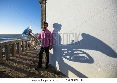 Young man play Tuba musical instrument near the white wall the shadow of the tool.