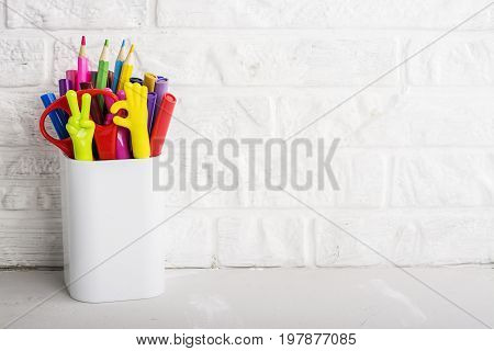 School background: a white brick wall with accessories, pencils, tetrads, scissors, an apple, pecans, a board for a substitute placed in front of her on the table. Selective focus