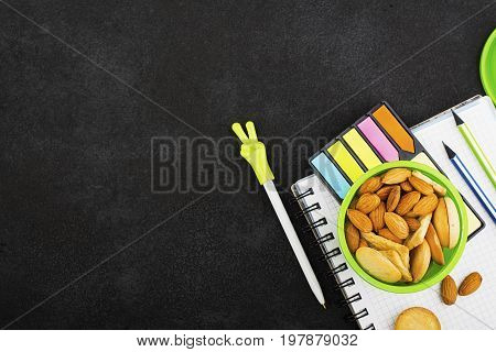 School lunch in a green round container with cookies and almonds on a dark background with handles and notebooks, pencils. Top View.