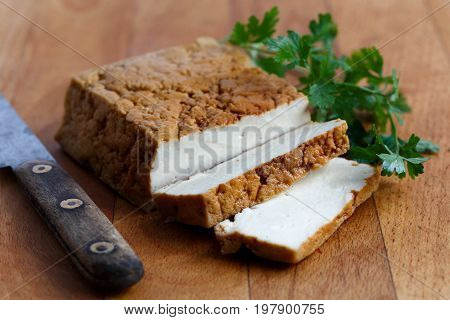 Block Of Smoked Tofu, Two Tofu Slices, Rustic Knife  And Fresh Parsley  On Wooden Chopping Board.