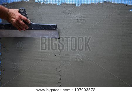 Hands Of An Old Manual Worker With Wall Plastering Tools Renovating House. Plasterer Renovating Outd