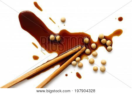 Spilled soya sauce and soya beans on white from above with chopsticks.