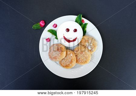 Pancakes on a plate with sour cream on a black background. Cheerful breakfast with a smile