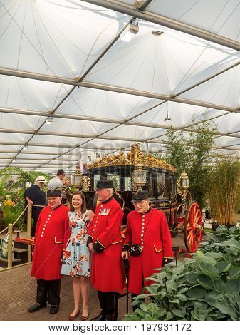 LONDON UK - MAY 25 2017: RHS Chelsea Flower Show 2017. Chelsea Pensioners pose with a young woman visitor near the Australian State Coach in the Great Pavilion.