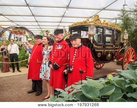LONDON UK - MAY 25 2017: RHS Chelsea Flower Show 2017. Chelsea Pensioners pose with a young woman visitor near the Australian State Coach in the Great Pavilion.