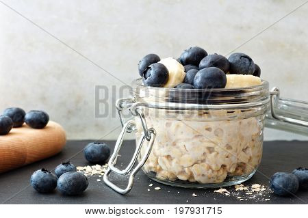 Jar Of Overnight Oats With Fresh Blueberries And Bananas, Scene With White And Black Stone Backgroun