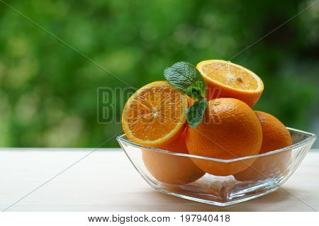 Glass bowl with oranges on a green background