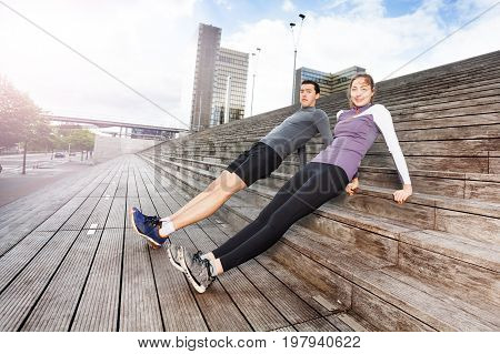 Sporty young couple holding correct position of reverse plank, exercising together outdoors on city stairs