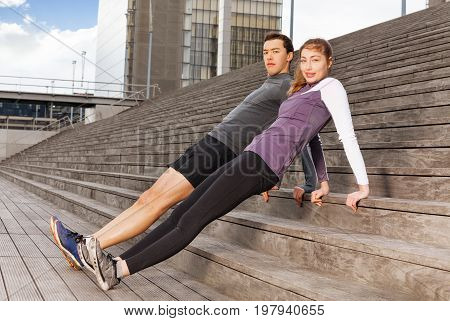 Portrait of active young people doing the reverse plank exercises outdoor on city stairs