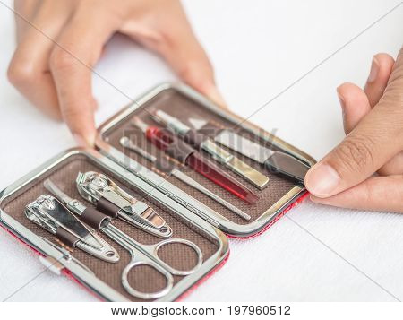 Closeup woman hand holding traveler's nail care kit of necessary tools set including scissors tweezers nail file and trimmer in red leather pocket case.