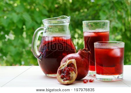 A jar and two glasses of pomegranate juice with ice and pomegranate.