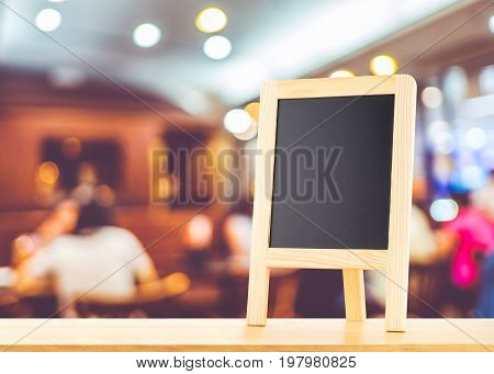 Blackboard with easel (menu board) on wooden table with blur bokeh restaurant backgroundMock up for display or montage of your content.