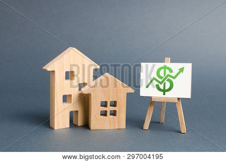 Wooden Figures Of Houses And A Poster With Green Arrow Up. The Concept Of Real Estate Value Growth. 