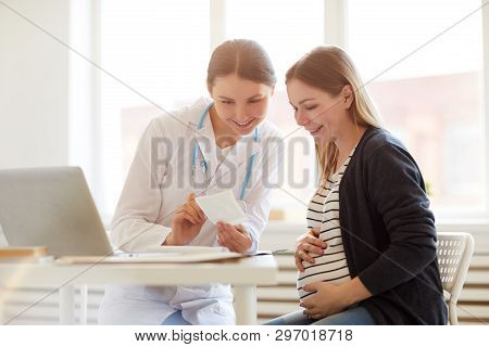Portrait Of Smiling Female Obstetrician Consulting Pregnant Woman In Doctors Office, Copy Space