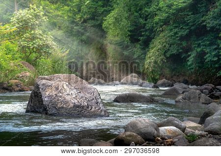 Deep Forest Stream Water Rushing By Big Rock In Middle River At Morning Sunshine And Warm Sunbeam Or